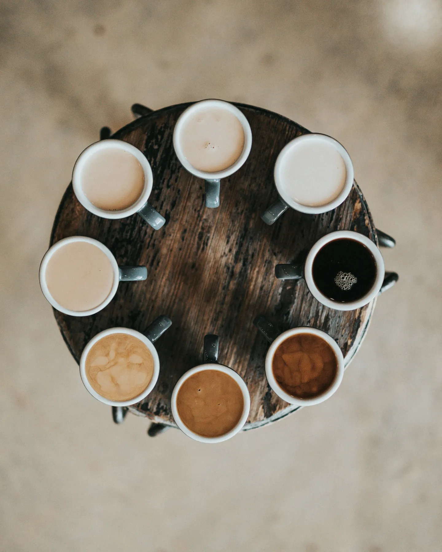 Vista cenital de ocho tazas de café servidas en círculo sobre una mesa redonda de madera